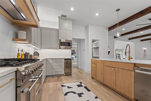 kitchen with pendant lighting, appliances with stainless steel finishes, wine cooler, beamed ceiling, and light wood-type flooring