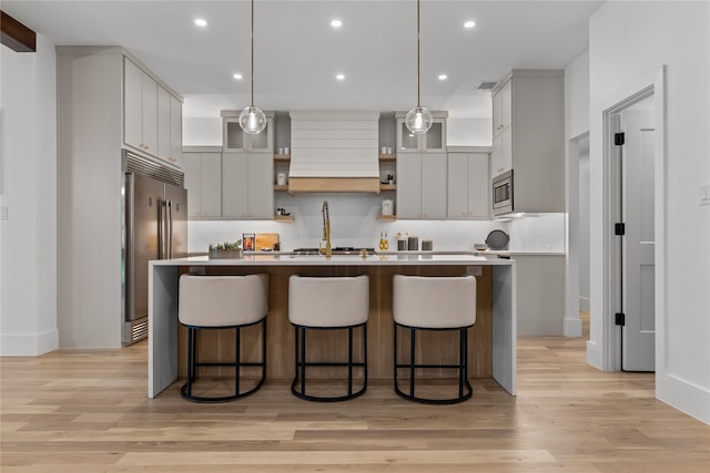 kitchen featuring light hardwood / wood-style flooring, appliances with stainless steel finishes, hanging light fixtures, an island with sink, and a kitchen bar