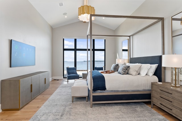 bedroom with light hardwood / wood-style floors, a water view, and high vaulted ceiling