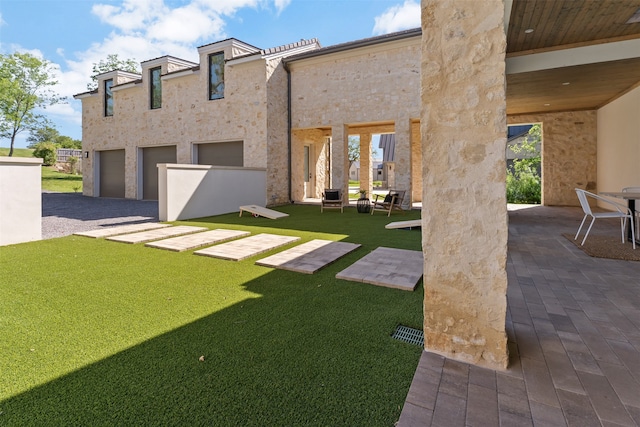 rear view of property featuring a garage, a patio, and a lawn