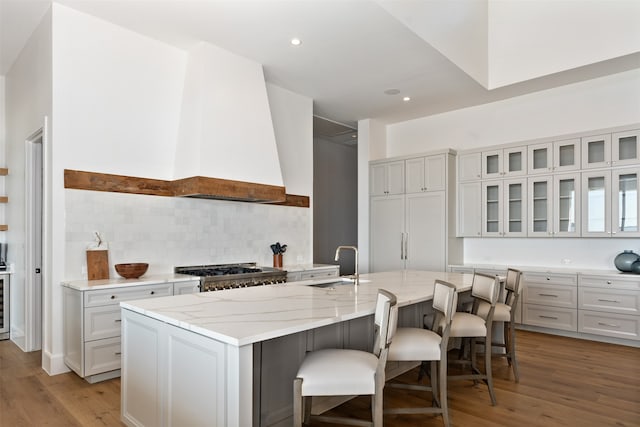 kitchen featuring tasteful backsplash, light wood-type flooring, a center island with sink, stove, and a kitchen breakfast bar