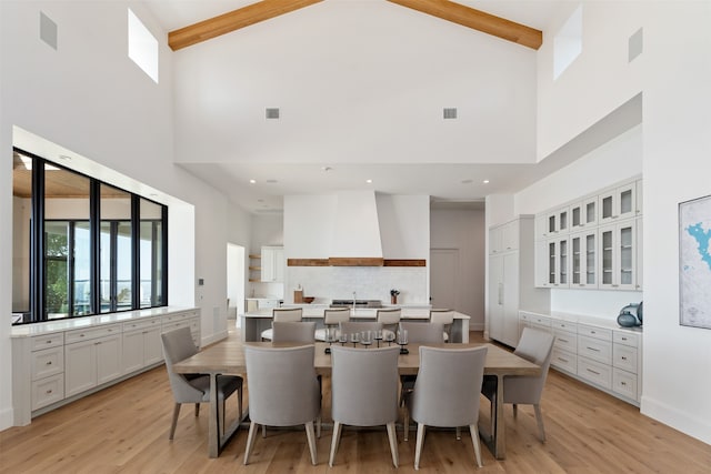 dining area featuring light wood-type flooring, beam ceiling, and high vaulted ceiling