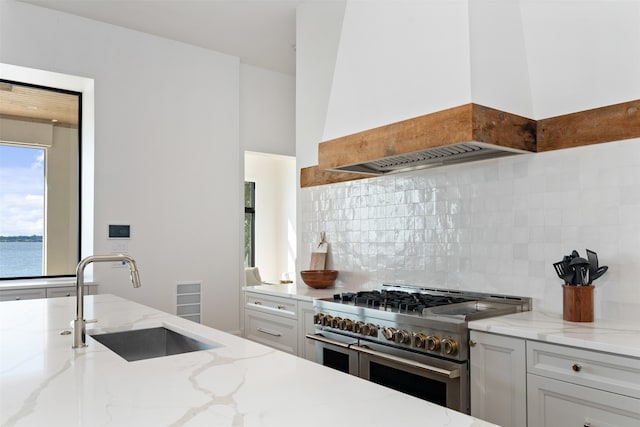 kitchen with decorative backsplash, white cabinetry, double oven range, and sink