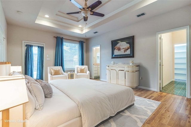 bedroom with ornamental molding, a tray ceiling, ensuite bathroom, and light wood-type flooring