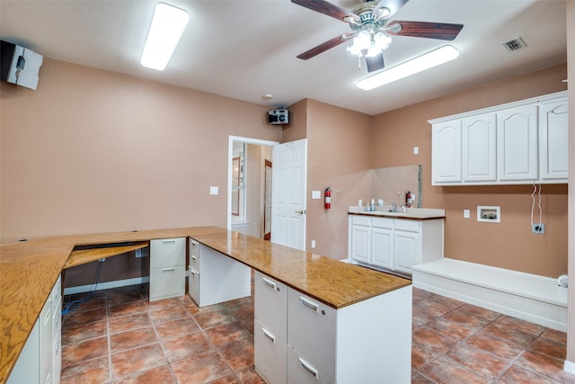 kitchen with ceiling fan, built in desk, kitchen peninsula, and white cabinets