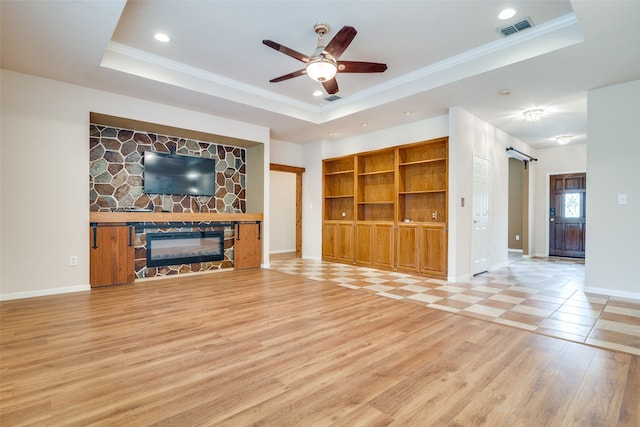 unfurnished living room with hardwood / wood-style floors, a tray ceiling, a fireplace, ornamental molding, and a barn door