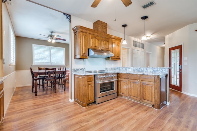 kitchen with light stone countertops, high end stove, light hardwood / wood-style floors, decorative light fixtures, and kitchen peninsula