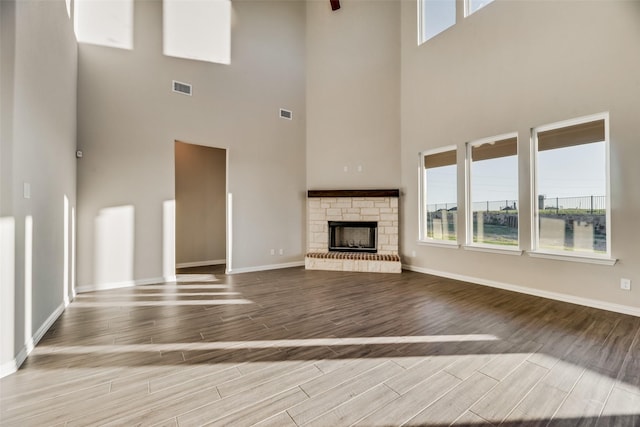 unfurnished living room with a towering ceiling, a fireplace, and light hardwood / wood-style flooring