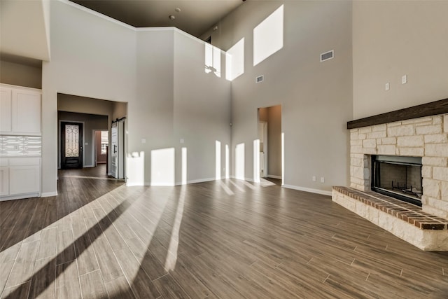 unfurnished living room featuring a stone fireplace, dark hardwood / wood-style flooring, a high ceiling, and a barn door