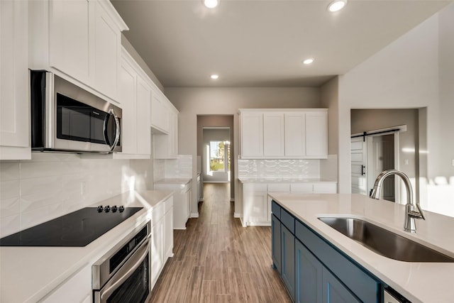 kitchen featuring a barn door, blue cabinets, white cabinetry, and appliances with stainless steel finishes