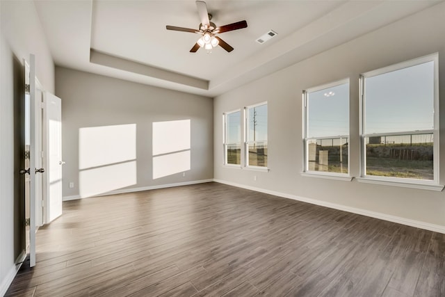 unfurnished room featuring a tray ceiling, ceiling fan, and dark wood-type flooring