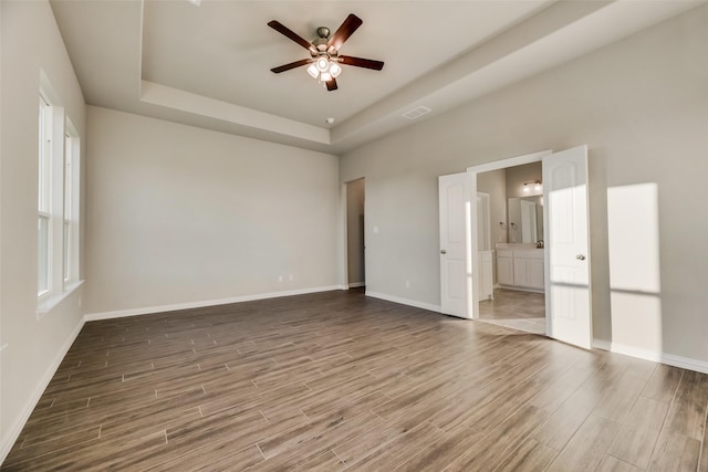 unfurnished bedroom with hardwood / wood-style floors, ceiling fan, a tray ceiling, and ensuite bath