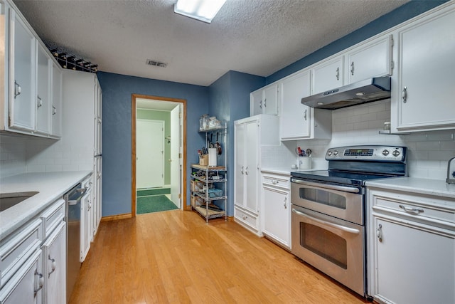 kitchen with backsplash, white cabinets, light wood-type flooring, and appliances with stainless steel finishes