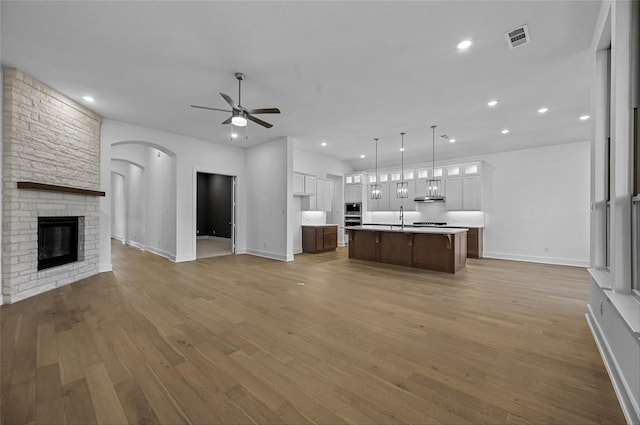 kitchen featuring a stone fireplace, wood-type flooring, white cabinetry, and a kitchen island with sink