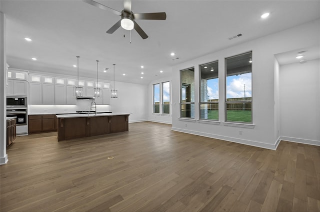 kitchen featuring hanging light fixtures, dark hardwood / wood-style floors, a kitchen island with sink, white cabinets, and appliances with stainless steel finishes