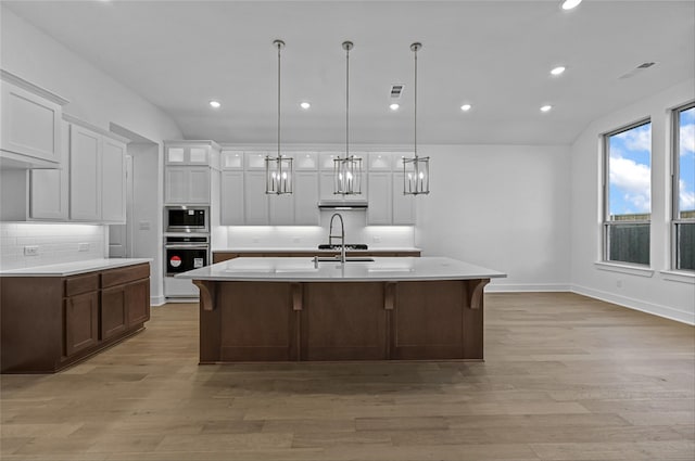 kitchen featuring an island with sink, decorative light fixtures, light hardwood / wood-style floors, white cabinetry, and stainless steel appliances