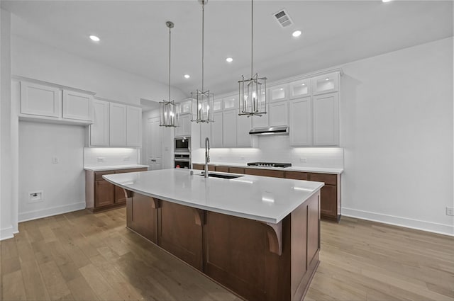 kitchen featuring light wood-type flooring, black gas stovetop, sink, a center island with sink, and white cabinetry