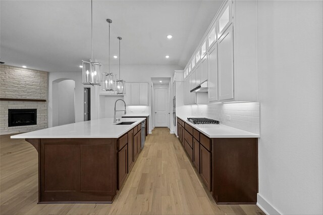 kitchen featuring white cabinetry, sink, a stone fireplace, light hardwood / wood-style flooring, and a large island with sink