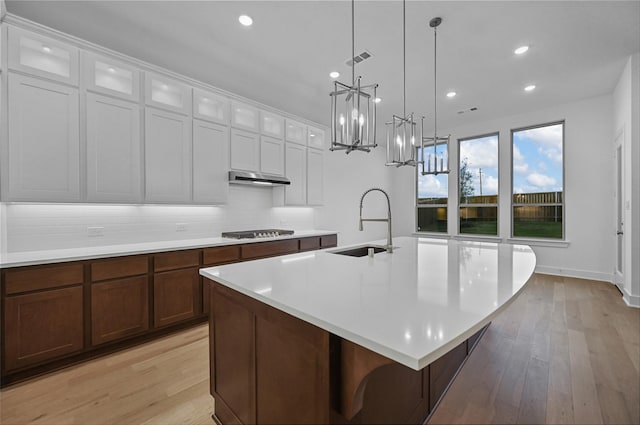 kitchen with a center island with sink, stainless steel gas stovetop, white cabinetry, and light hardwood / wood-style flooring