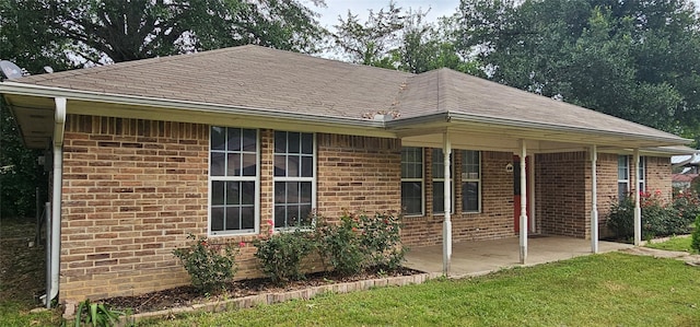 exterior space featuring a patio, roof with shingles, a lawn, and brick siding