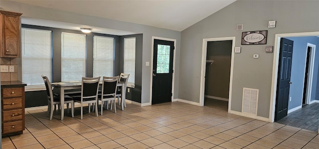 dining area with light tile patterned floors, visible vents, vaulted ceiling, and baseboards