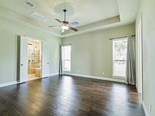 unfurnished bedroom with ceiling fan, dark hardwood / wood-style flooring, connected bathroom, and a tray ceiling