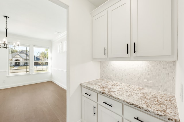 bar featuring tasteful backsplash, white cabinetry, a chandelier, light hardwood / wood-style floors, and light stone countertops