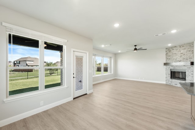 unfurnished living room with ceiling fan, a stone fireplace, and light hardwood / wood-style flooring