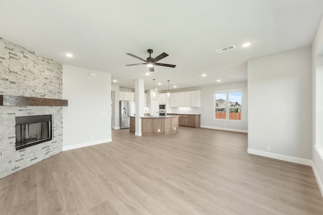 unfurnished living room with light wood-type flooring, a stone fireplace, and ceiling fan