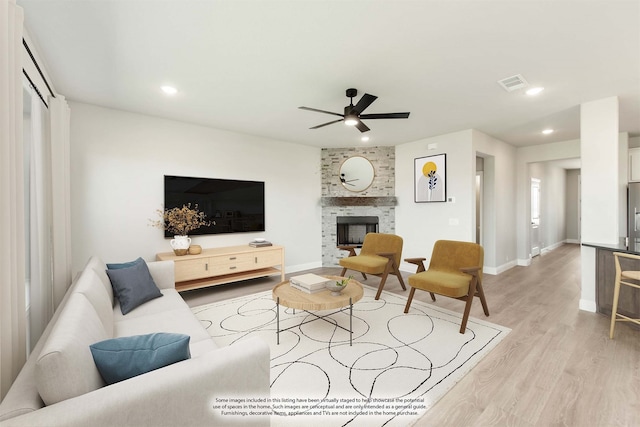 living room featuring a large fireplace, light hardwood / wood-style flooring, and ceiling fan