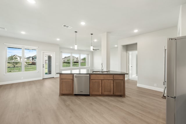 kitchen featuring appliances with stainless steel finishes, an island with sink, pendant lighting, light hardwood / wood-style flooring, and sink