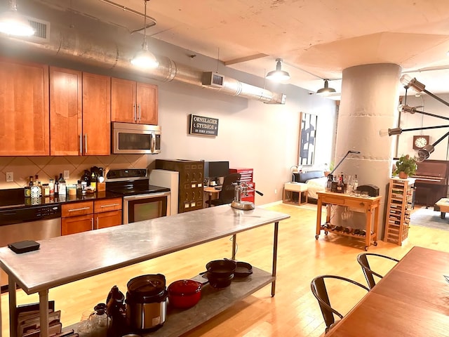 kitchen with decorative backsplash, pendant lighting, light wood-type flooring, and stainless steel appliances