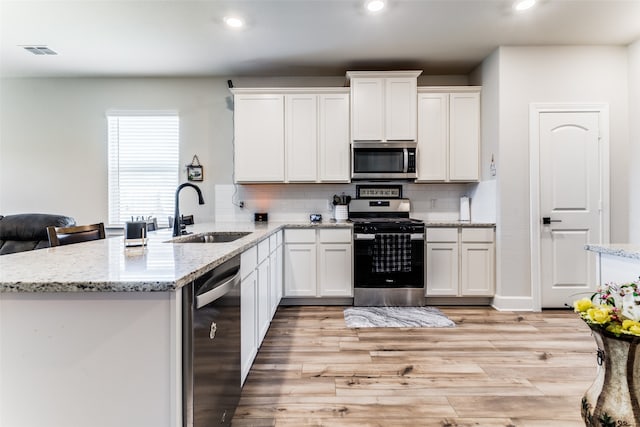 kitchen featuring light hardwood / wood-style floors, kitchen peninsula, backsplash, sink, and appliances with stainless steel finishes