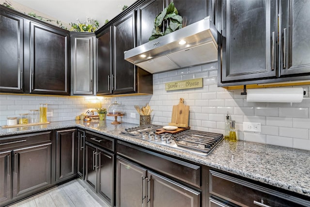 kitchen with stainless steel gas stovetop, tasteful backsplash, light stone counters, and range hood