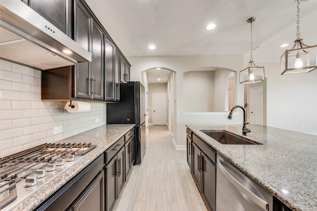 kitchen featuring sink, extractor fan, appliances with stainless steel finishes, pendant lighting, and light stone countertops