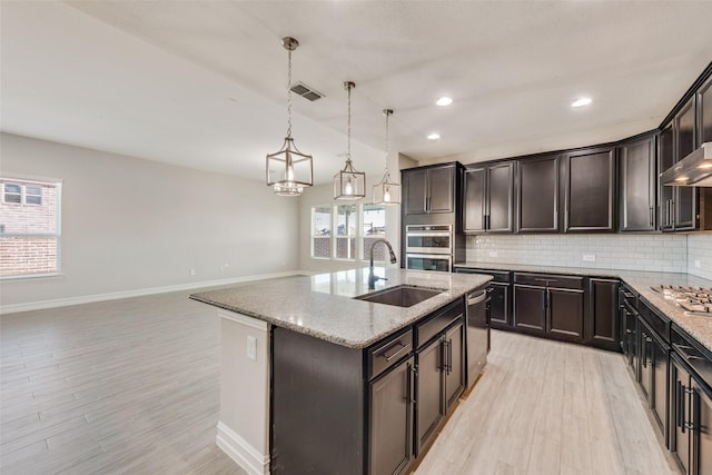 kitchen featuring sink, light stone counters, an island with sink, pendant lighting, and backsplash