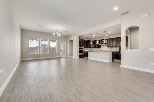 unfurnished living room with an inviting chandelier, sink, and light wood-type flooring