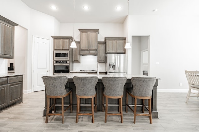 kitchen with a kitchen island with sink, a kitchen breakfast bar, hanging light fixtures, light stone counters, and stainless steel appliances