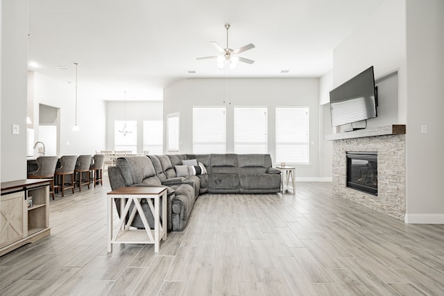 living room with a fireplace, ceiling fan, plenty of natural light, and light wood-type flooring