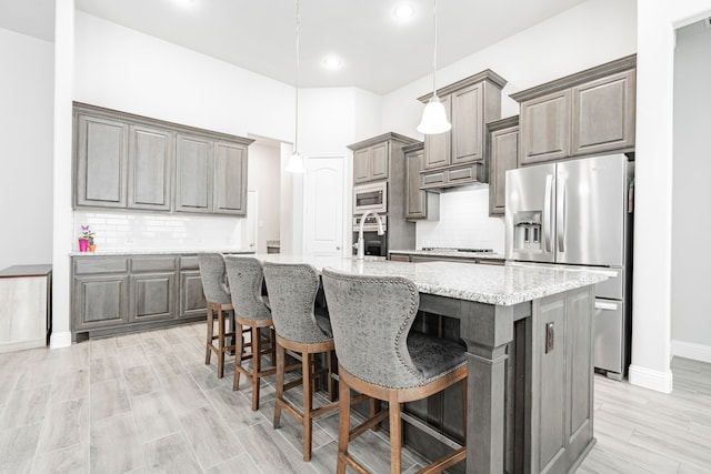 kitchen featuring decorative light fixtures, a kitchen island with sink, appliances with stainless steel finishes, and tasteful backsplash