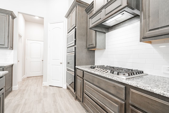 kitchen featuring dark brown cabinetry, tasteful backsplash, light hardwood / wood-style flooring, custom range hood, and appliances with stainless steel finishes