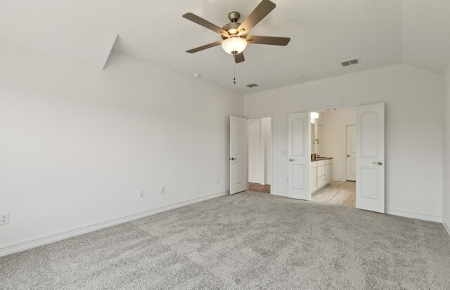 unfurnished bedroom featuring ceiling fan, light colored carpet, connected bathroom, and vaulted ceiling