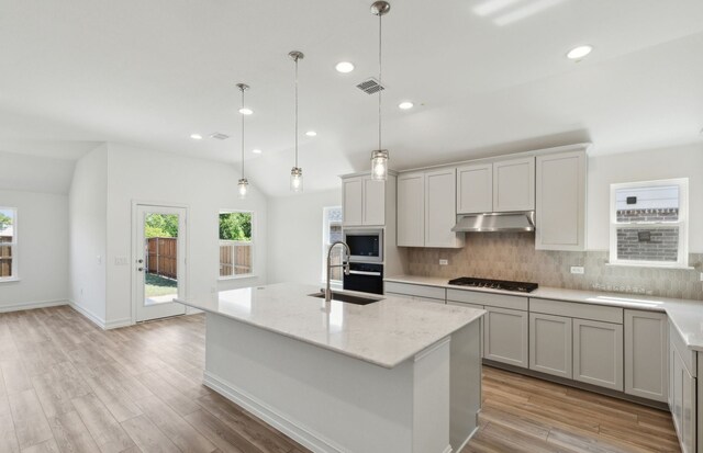 kitchen with sink, an island with sink, vaulted ceiling, and appliances with stainless steel finishes