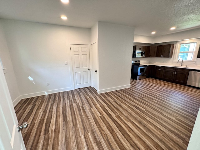 kitchen featuring light countertops, appliances with stainless steel finishes, a sink, dark brown cabinets, and wood finished floors