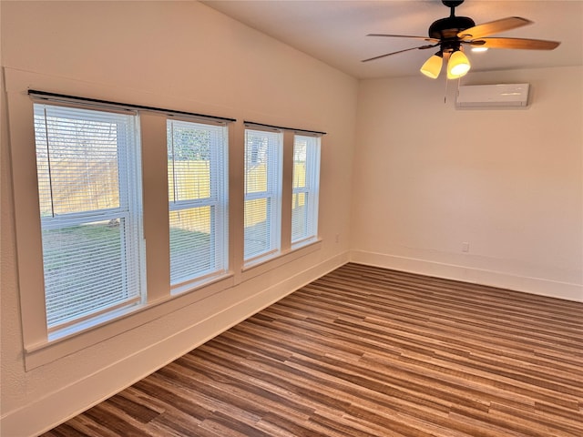 spare room with a wall unit AC, dark wood-style floors, ceiling fan, and baseboards