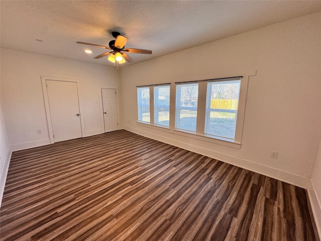 unfurnished room featuring a textured ceiling, dark wood-style flooring, a ceiling fan, and baseboards