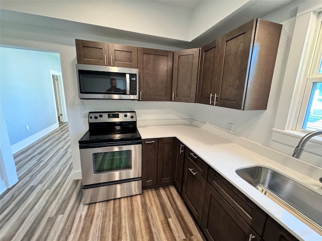 kitchen featuring stainless steel appliances, light countertops, light wood-style floors, a sink, and dark brown cabinets