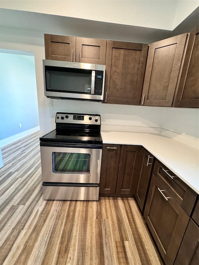 kitchen featuring dark brown cabinetry, light wood-style flooring, appliances with stainless steel finishes, and light countertops