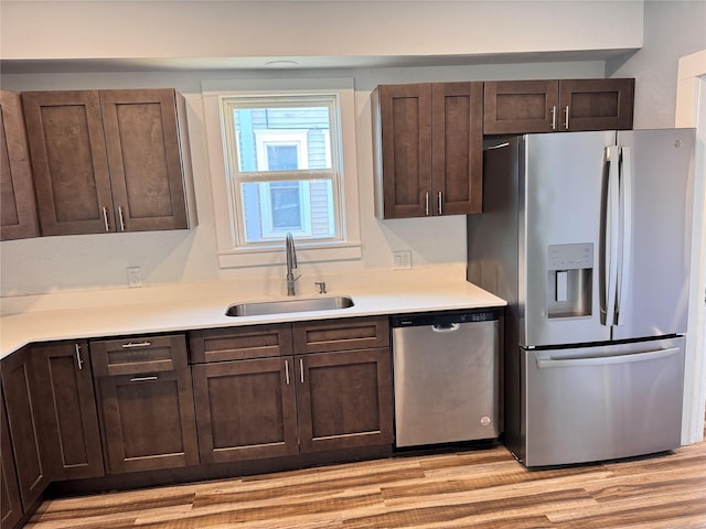 kitchen with stainless steel appliances, a sink, light countertops, and light wood-style floors