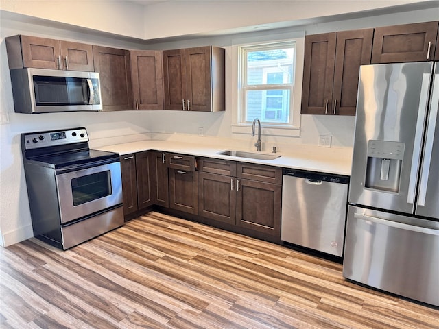 kitchen with light wood finished floors, appliances with stainless steel finishes, a sink, and dark brown cabinetry